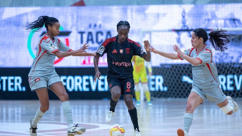 Jogadora do Benfica tenta passar pelas adversárias durante jogo de futsal