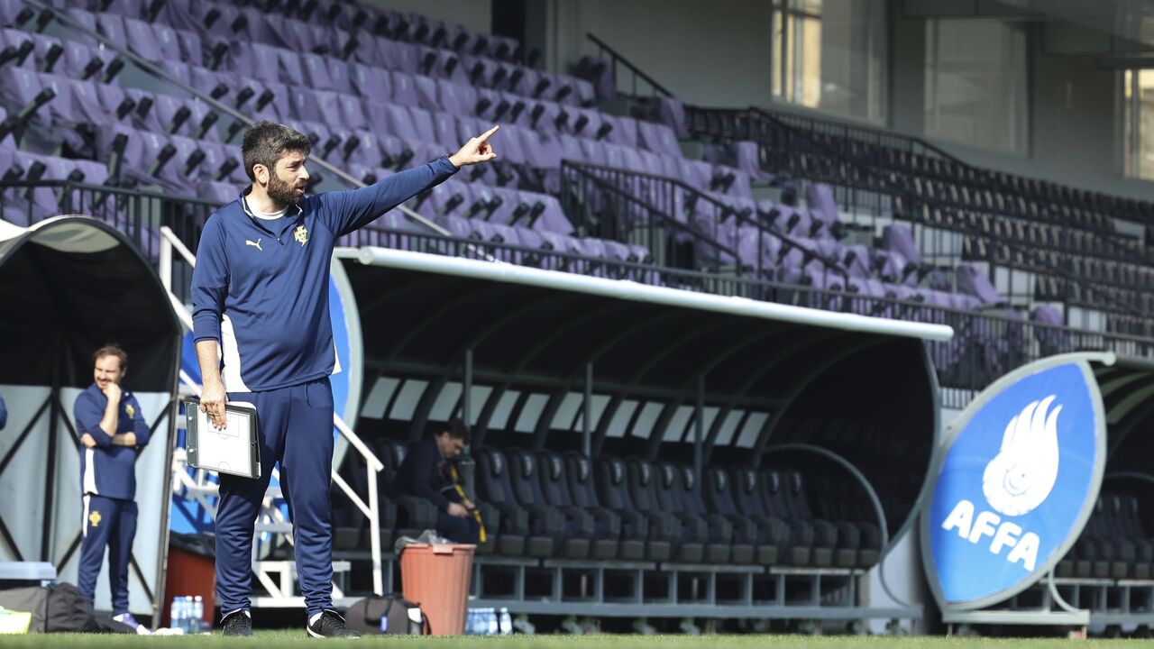 Um treinador de futebol gesticula no relvado, perto do banco de suplentes