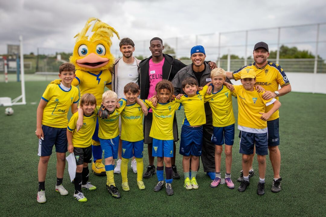 Grupo de crianças e adultos posa num campo de futebol