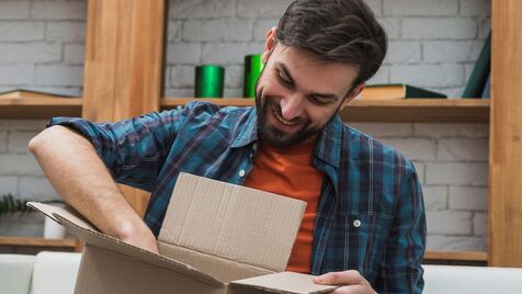 Homem sorri ao abrir uma caixa em casa