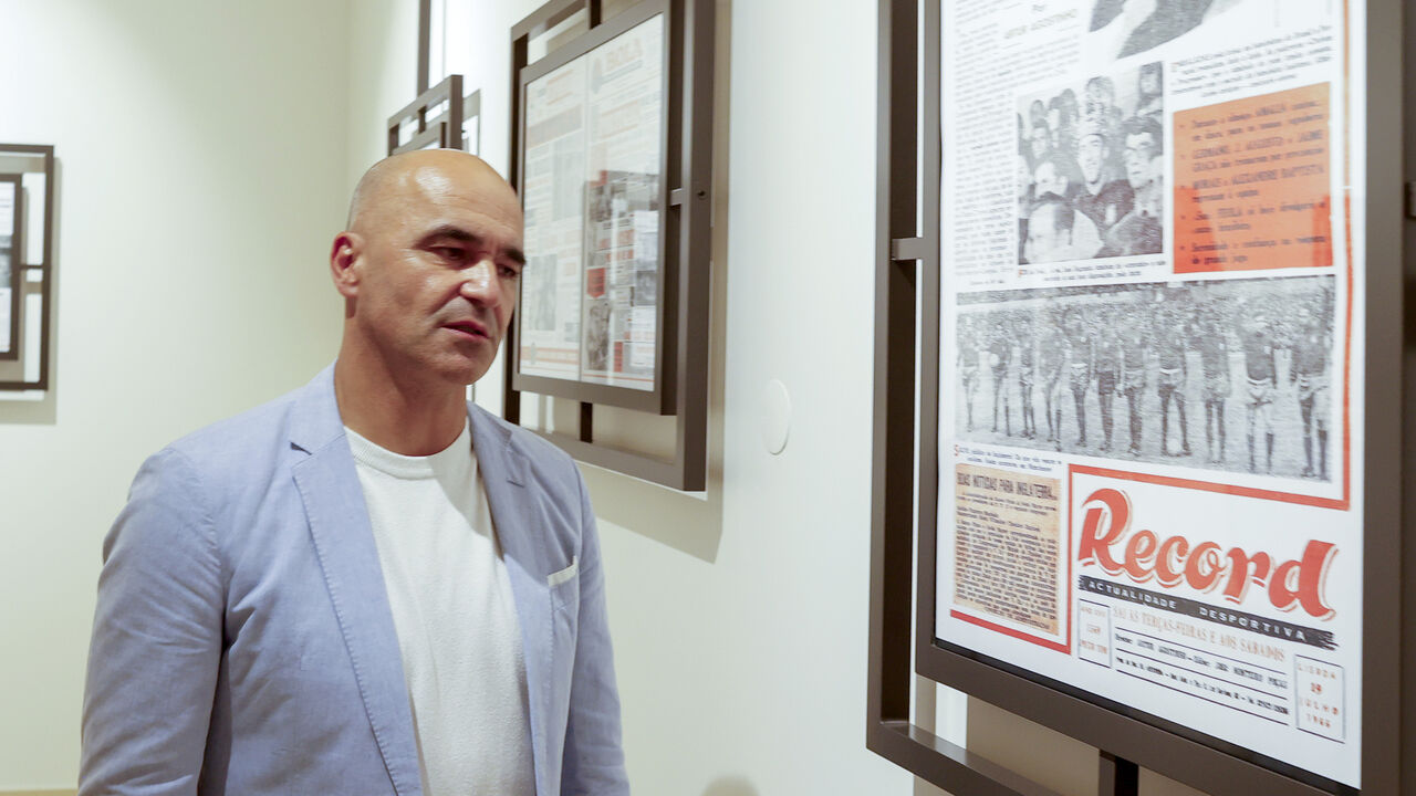 Homem observa capas do jornal Record numa exposição.
