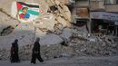 Palestinianos passam por edifícios destruídos