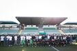 Grupo de futebol posa num estádio com adeptos e equipa técnica
