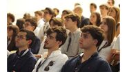 Pessoas assistem a evento em espaço fechado com atenção