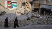 Palestinianos passam por edifícios destruídos