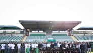 Grupo de futebol posa num estádio com adeptos e equipa técnica