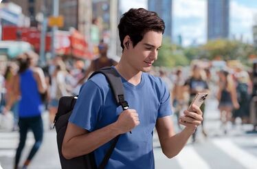 Homem usa auriculares e vê telemóvel na rua