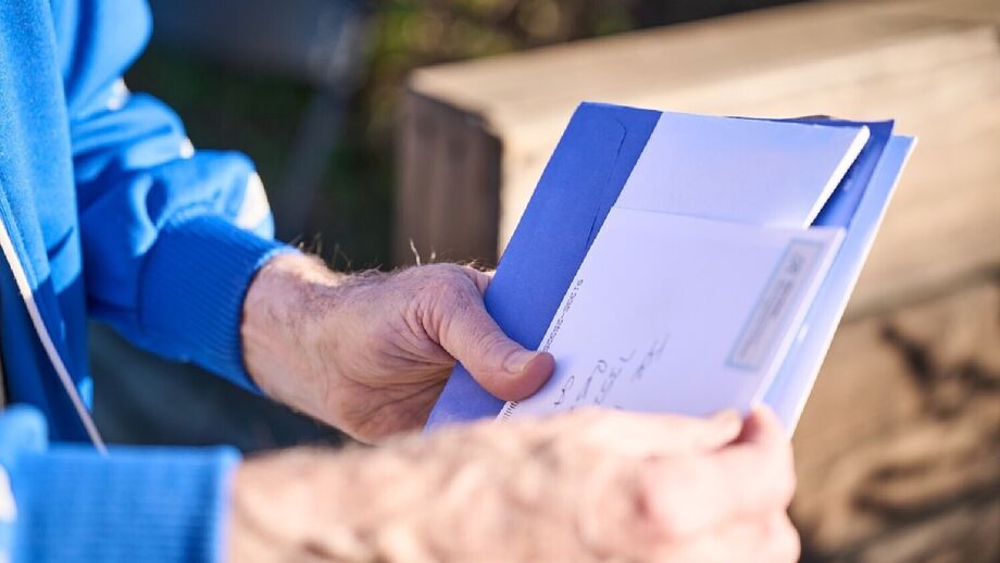 Homem lê correspondência com envelope azul e conteúdo branco