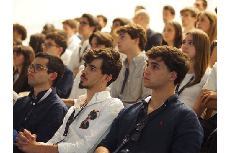 Pessoas assistem a evento em espaço fechado com atenção