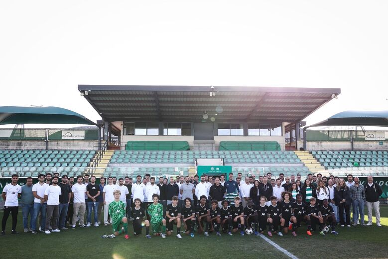 Grupo de futebol posa num estádio com adeptos e equipa técnica