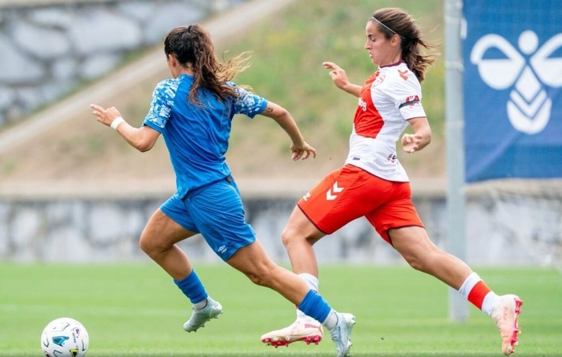 Duas jogadoras disputam a bola num campo de futebol