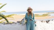 Modelo com chapéu de palha e conjunto de calças e camisa azul turquesa, junto ao mar