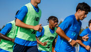 Jogadores de futebol em treinamento com coletes verdes e camisetas azuis