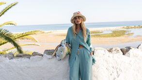 Modelo com chapéu de palha e conjunto de calças e camisa azul turquesa, junto ao mar