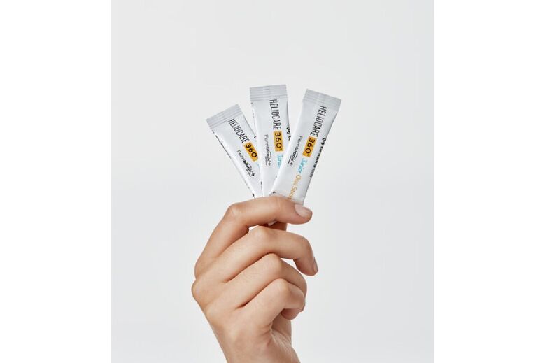 Mão segura 3 ampolas de Heliocare 360º Junior Oral Sticks