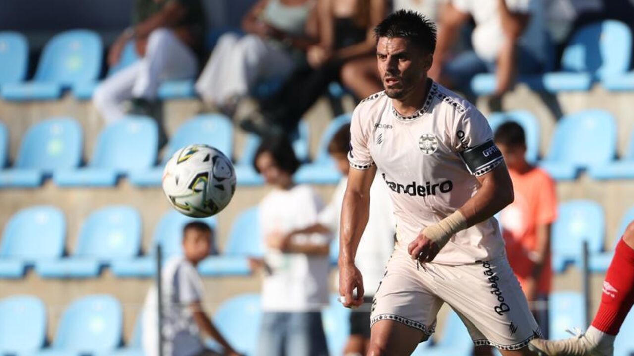 Dois jogadores de futebol disputam a bola, um deles com uma ligadura na cabeça
