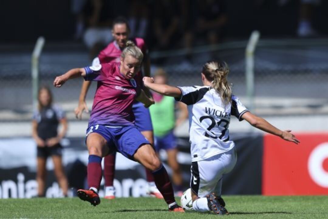 Duas jogadoras de futebol disputam a bola em campo