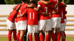 Jogadores de futebol de braços dados em círculo no campo
