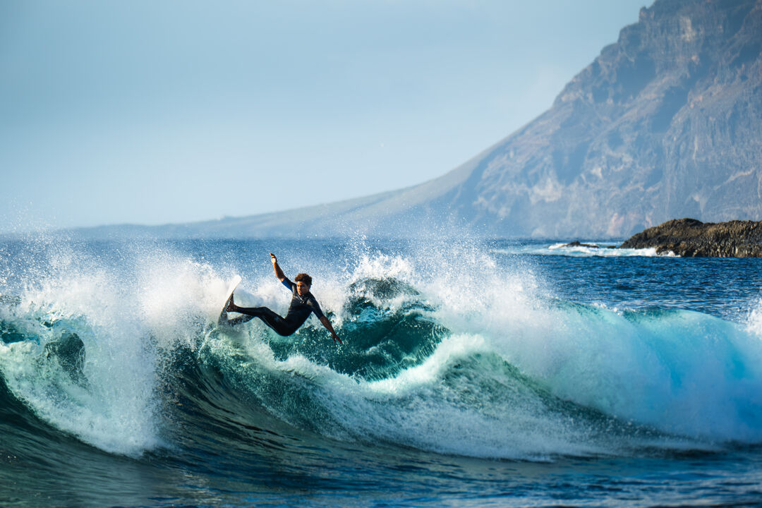 Surfista em Tenerife desliza numa onda com montanhas ao fundo