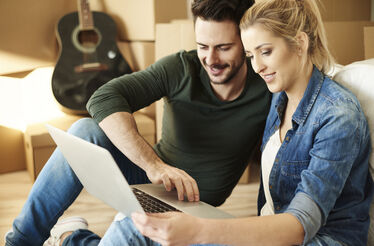 Casal analisa computador rodeado de caixas e guitarra, enquanto ofertas terminam