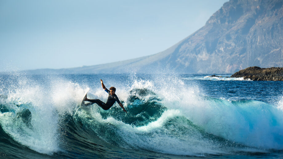 Surfista em Tenerife desliza numa onda com montanhas ao fundo